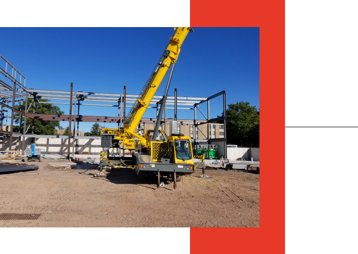 Group 1321317408 A yellow crane at a construction site with steel beams.
